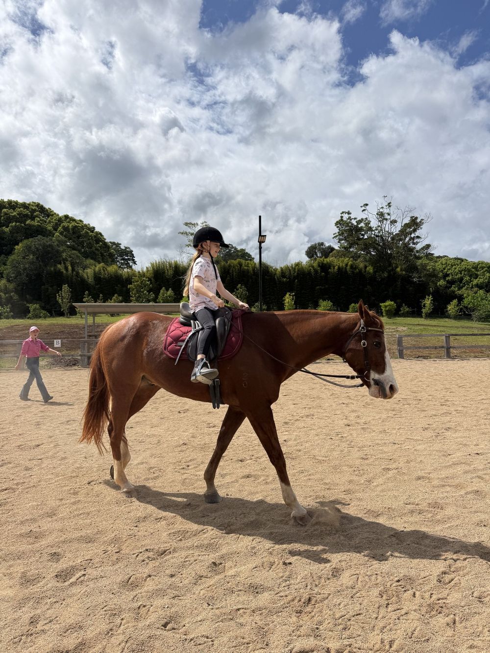 Girl riding a chestnut, instructor nearby